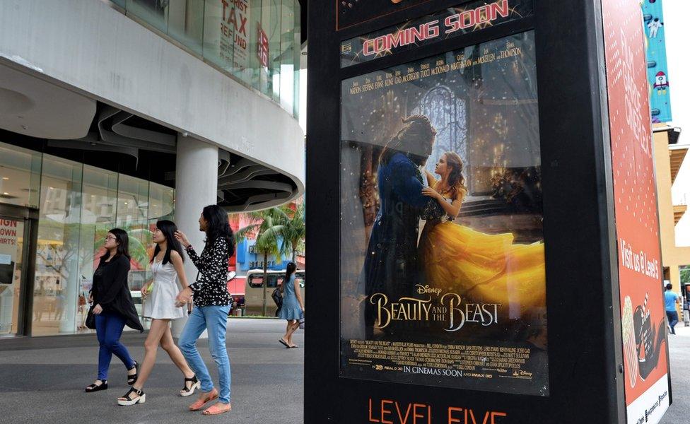 People walk past a poster for the film Beauty and the Beast in Singapore on 14 March 2017.