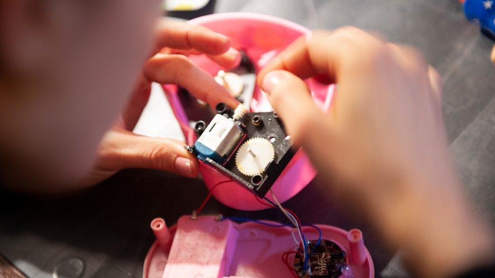 A woman is repairing or tinkering with an electronic toy which she has opened