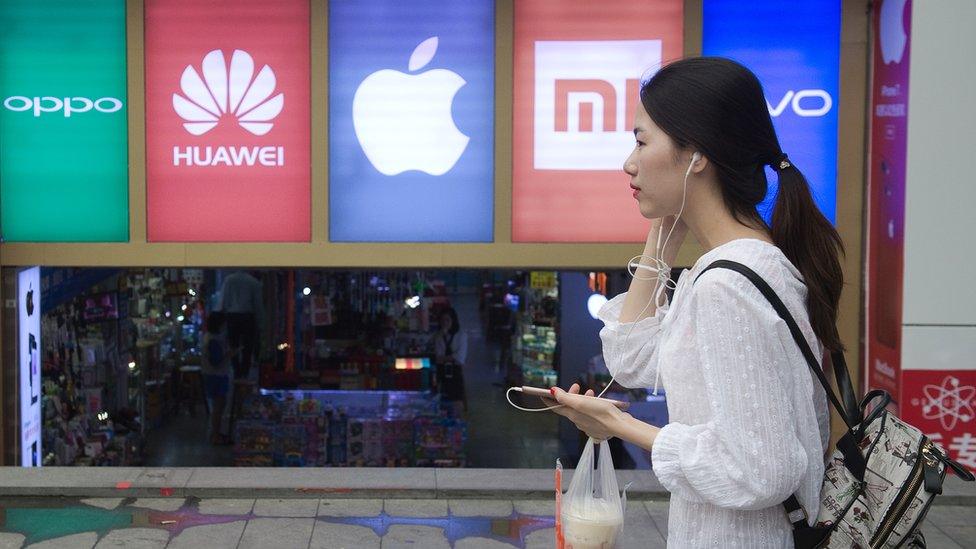 Woman walks past several mobile phone brand signs