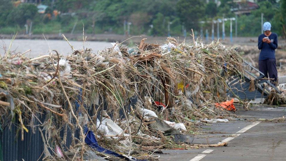 Man checks his phone next to debris at Xindian river banks in Taipei, Taiwan (29 Sept 2015)