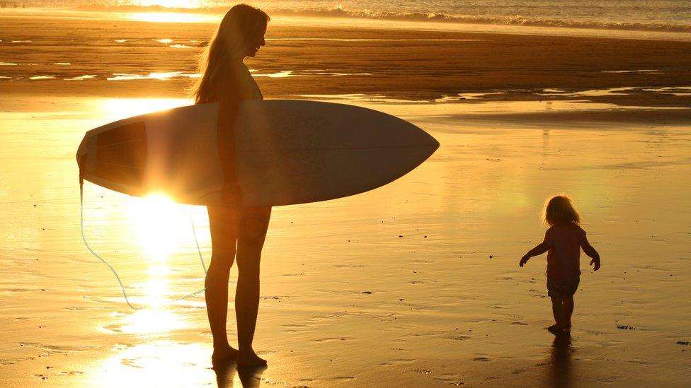 Woman surfer and toddler on beach