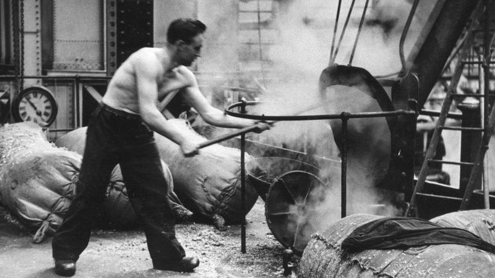 A worker at the Guinness brewery at Saint Jame's Gate, Dublin, clearing a chute. 1953