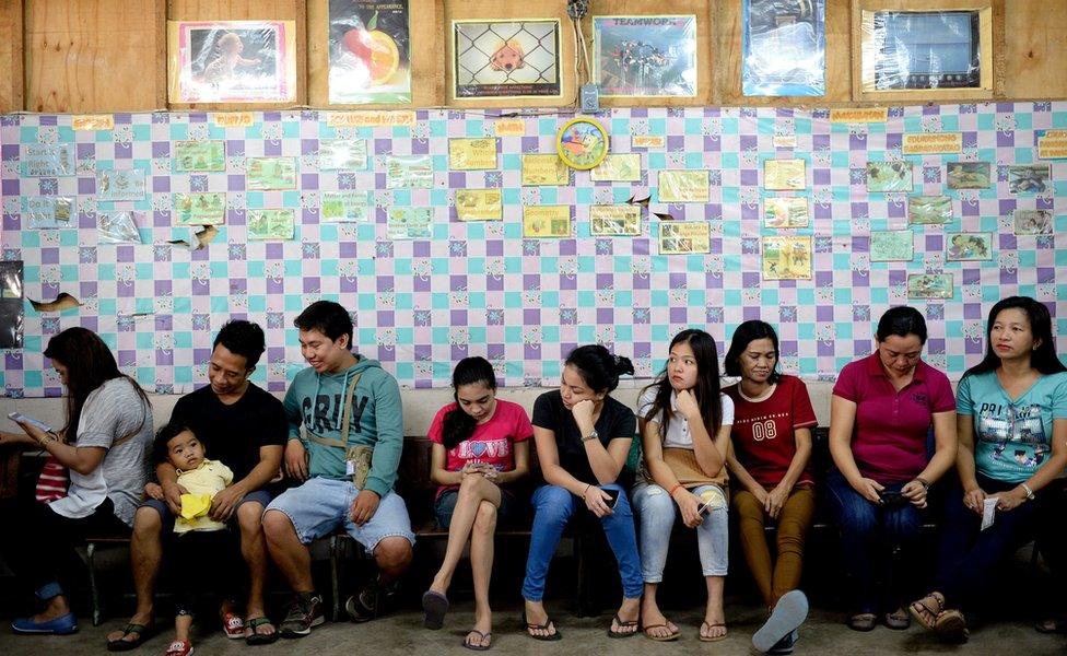 A line of voters of different ages and genders, seated while they wait to vote, in a polling station in Davao