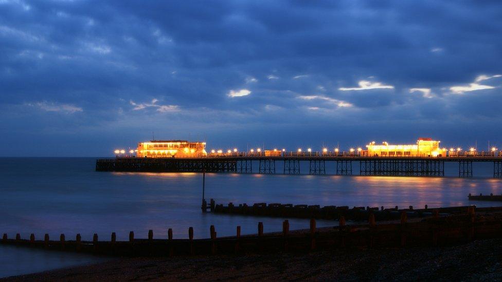 The illuminated pier glows against a cloudy evening sky