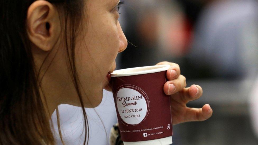 A woman drinks coffee in a cup bearing the sign of the summit between the US and North Korea in Singapore, 10 June