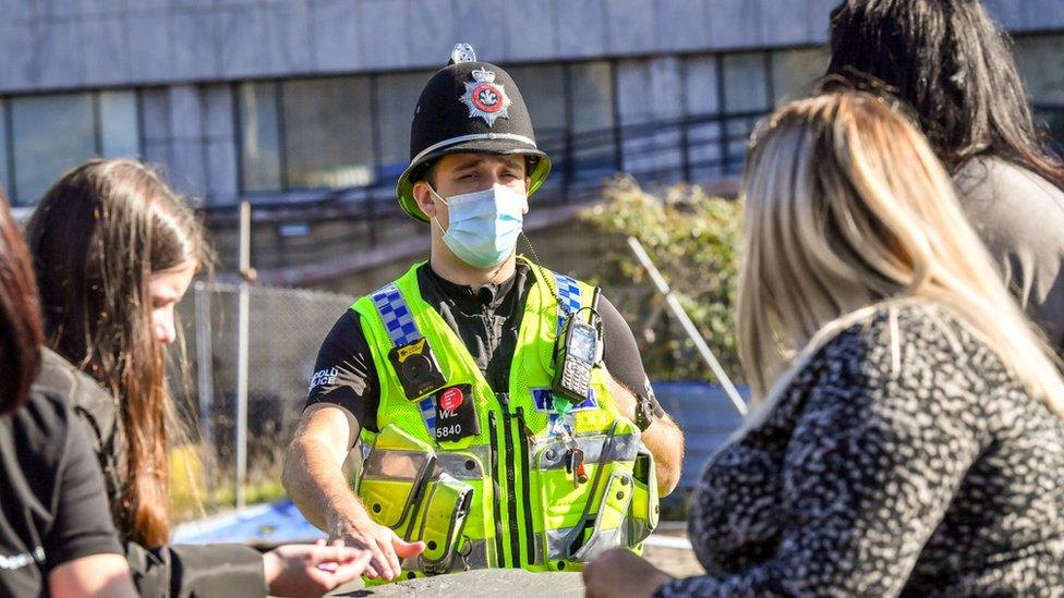 Police officer in high-vis vest and police helmet talks to lockdown demonstrators holding a protest in Cardiff Bay, Cardiff