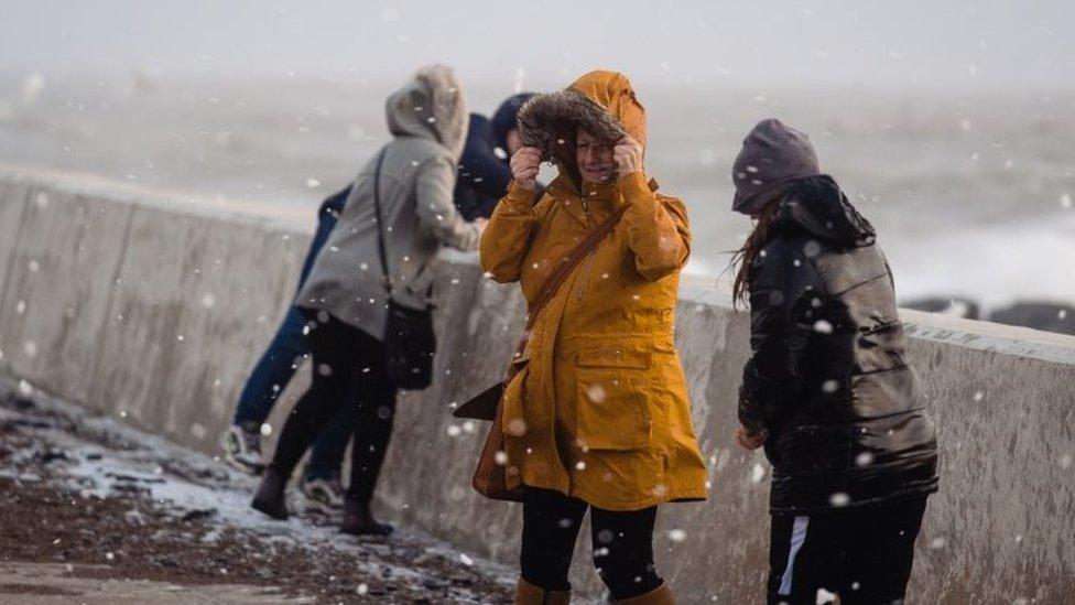 People walk through flying sea foam spray on Sunday in Porthcawl, Wales