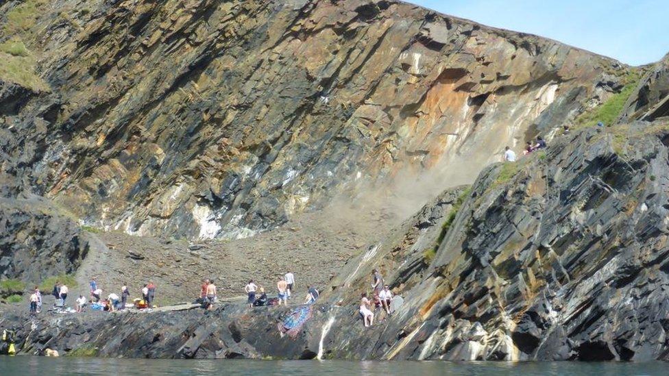 People looking at a landslip near a blue lagoon