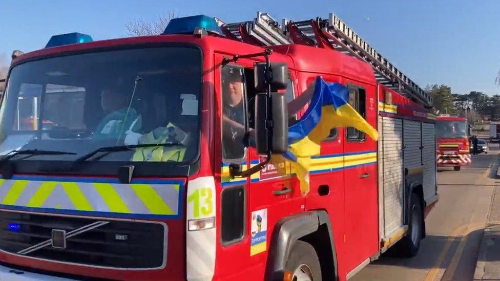 A Ukraine flag being waved from the window of a fire engine