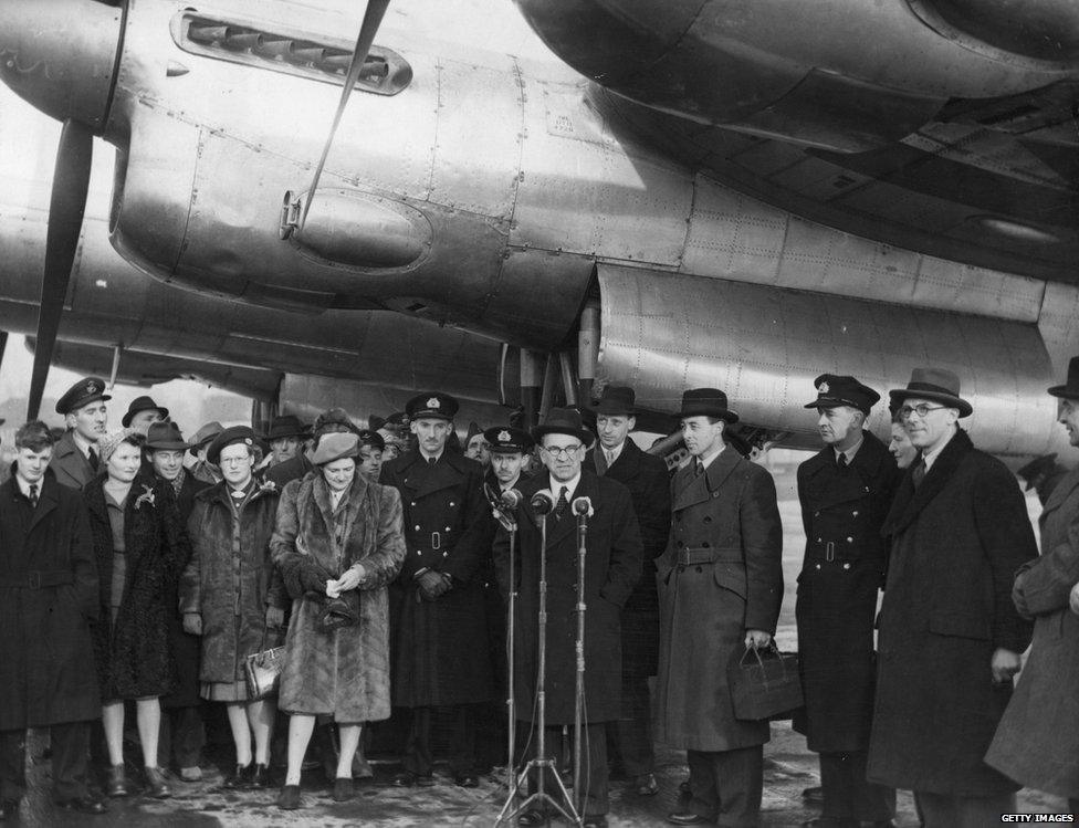 Lord Winster, Minister of Civil Aviation, making an address at Heathrow Airport, London beside Air Vice Marshal Donald Bennett (right), who formed and led the RAF's Pathfinder Force. Bennett will mark the transfer of the airport from military to civil control by taking off in the Lancastrian airliner Starlight (in background) on a survey flight to South America, 1946