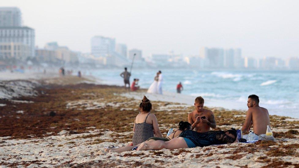 Tourists are seen on a beach covered wth seaweed in Cancun