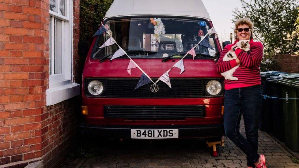 A woman poses with her dog next to her campervan