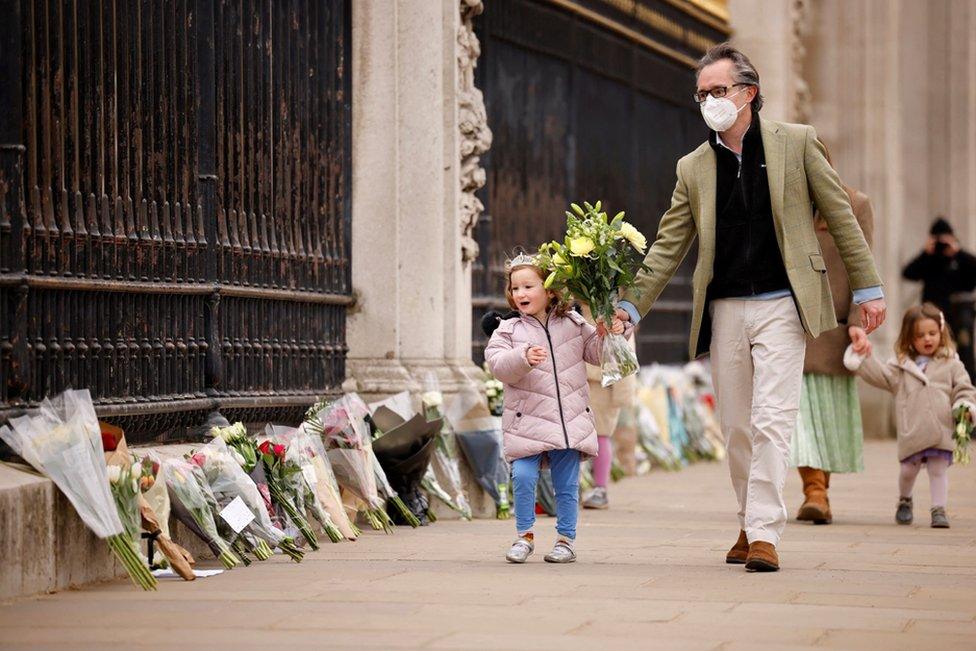 A child carries a floral tribute to Britain's Prince Philip, Duke of Edinburgh outside Buckingham Palace, central London on 10 April 2021