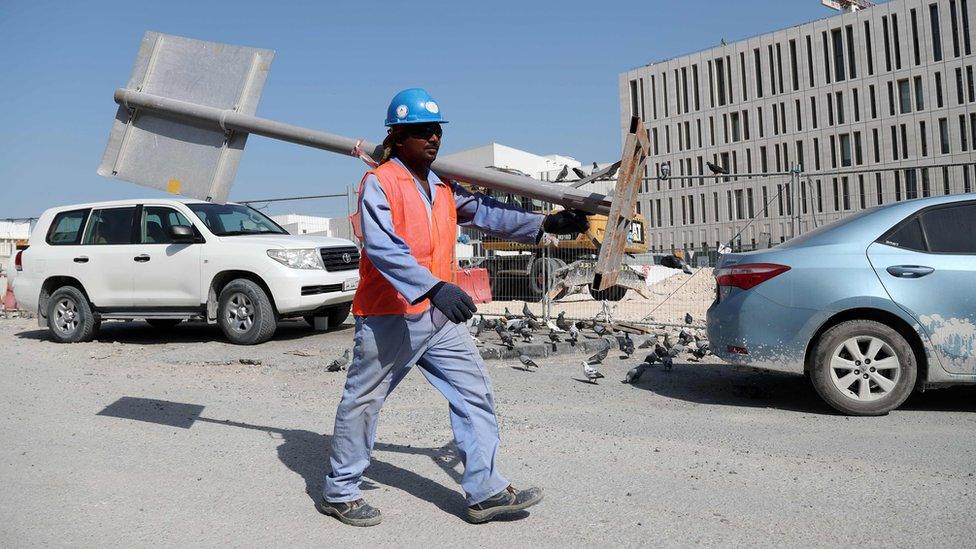 A migrant worker carrying a pole at a construction site in the Qatari capital Doha