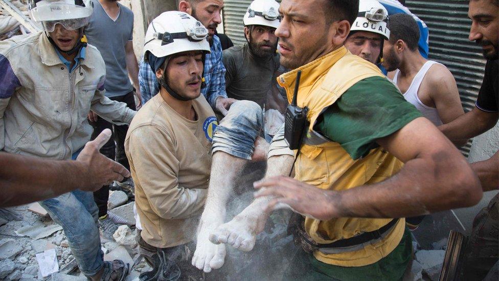 July 23, 2016 shows Syrian civil defence volunteers, known as the White Helmets, carrying a body after digging it out from under the rubble of a building following a reported airstrike