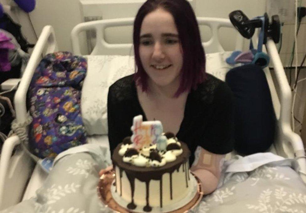 Charlotte holding a birthday cake, in her hospital bed