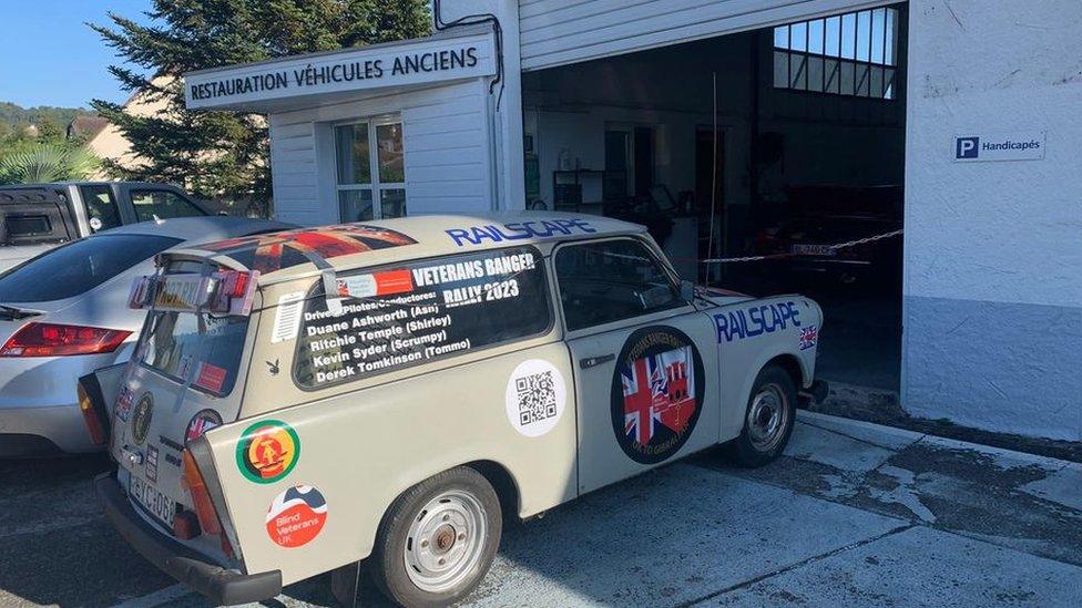 Green-coloured Trabant with team names in the window drives into a roadside garage