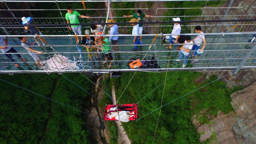 The couple suspended off Shiniuzhai glass bridge, watched by passersby and people organising their suspension, 9 August 2016