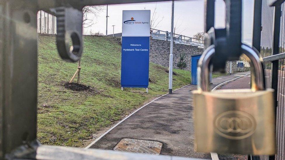 Sign that Reads: "Driver & Vechile Agency Welcome to Hydebank Test Centre" behind a padlock