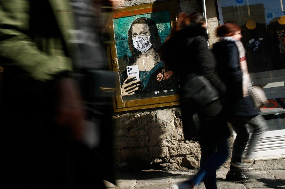 People walk by a poster by Italian urban artist Salvatore Benintende aka "TVBOY" depicting Leonardo da Vinci's Mona Lisa wearing a protective facemask and holding a mobile phone, 18 February 2020.