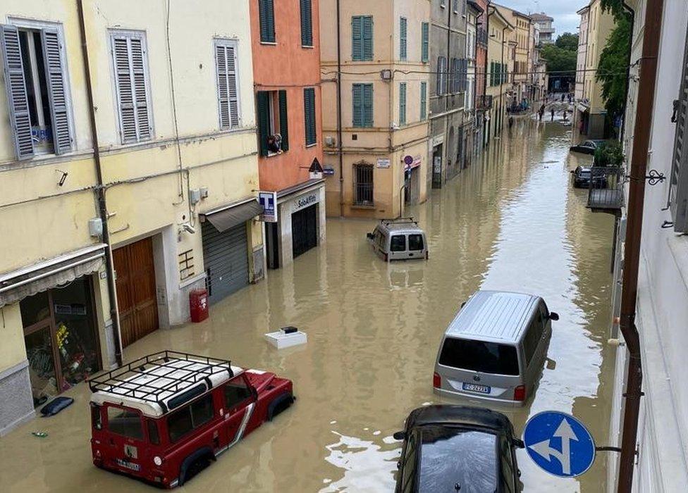 A flooded street with several cars with water reaching to above their wheels