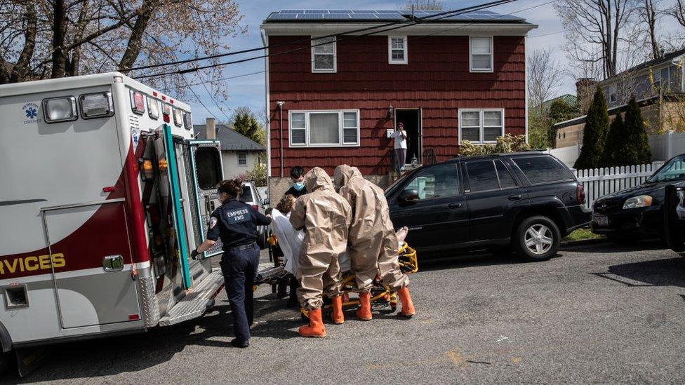 Yonkers Fire Department EMTs, clothed in full personal protective equipment (PPE), assist Empress EMS EMTs to transport a patient with COVID-19 symptoms to a hospital on 14 April, 2020