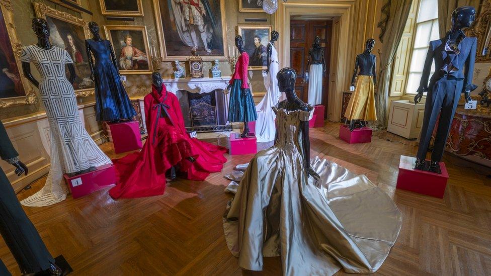 mannequins wearing dresses in a room with paintings on the wall