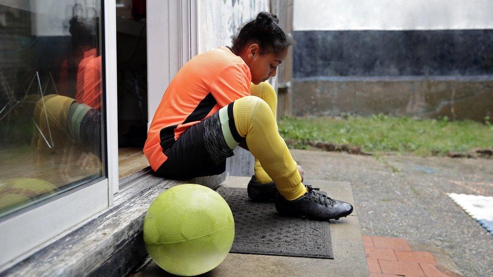 Girls tying football boots up sitting on a step with the ball beside her.
