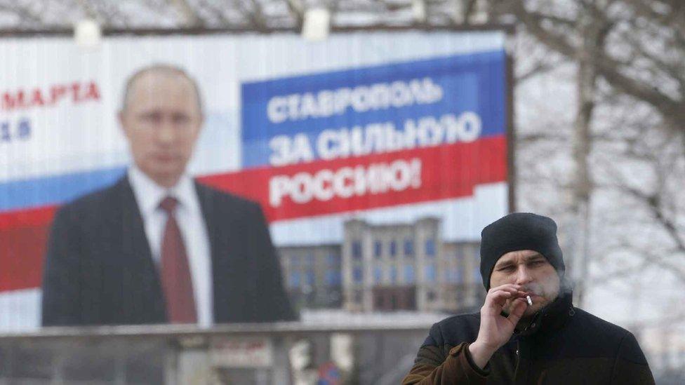 Man smokes cigarette in front of Putin election poster