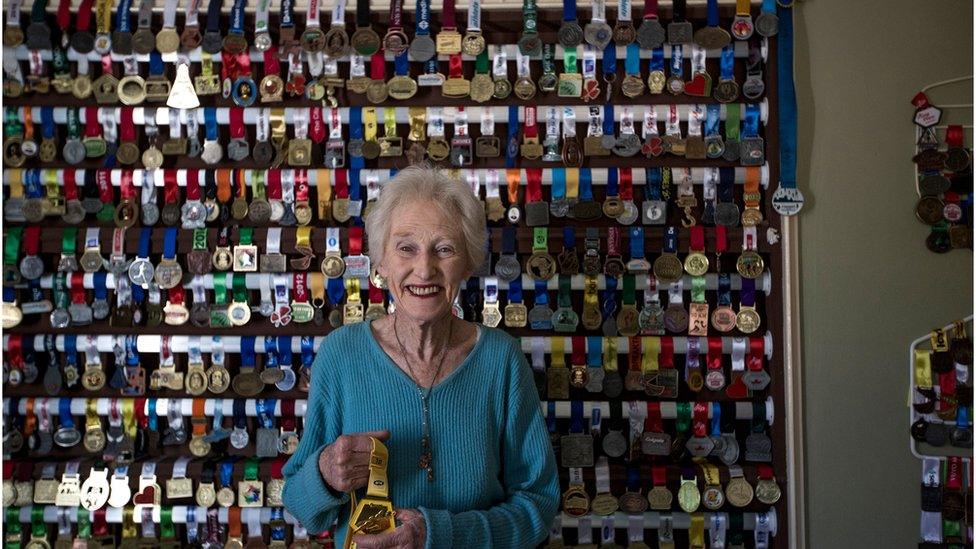 Deirdre Larkin stands in front of a wall with her medals on it.