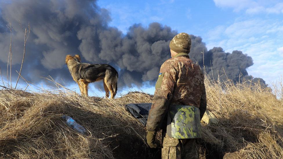 A Ukrainian serviceman and his dog look at smoke from a burned petroleum storage depot damaged after a Russian missile attack near Kyiv on 27 February 2022