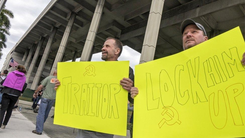 Protesters holding signs saying: "lock him up" and "traitor"