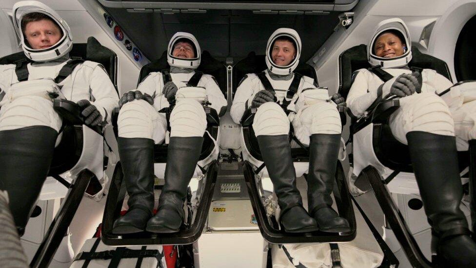 Four astronauts strapped into their seats in a capsule ready to go to space