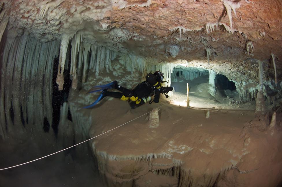 Xisco Gracia swimming through a cave. His torch lights up a guideline