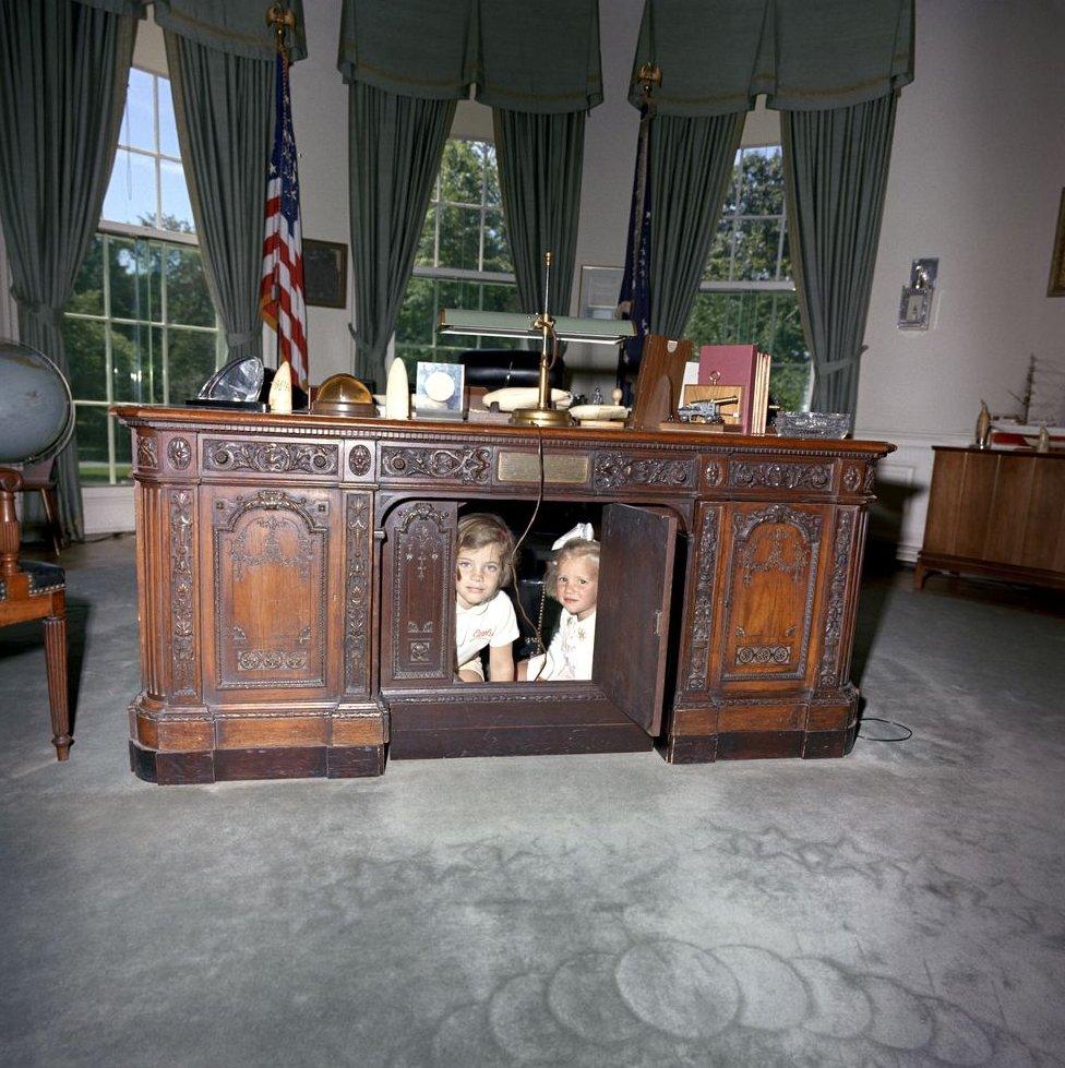 Caroline Kennedy and Kerry Kennedy, daughter of Attorney General Robert F. Kennedy, look through hinged panel of President John F. Kennedy's desk (HMS Resolute Desk) in the Oval Office, White House, Washington, D.C.