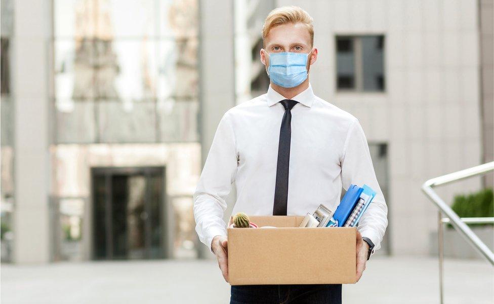 Stock image of a man in facemask carrying a box of his belongings from the office