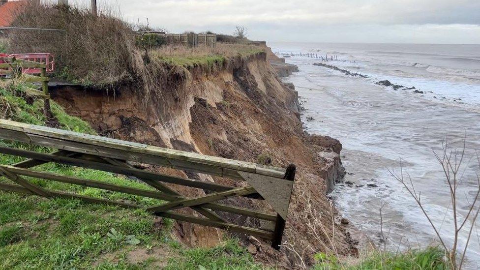 A farm gate hangs over the edge of the crumbling cliff at Happisburgh