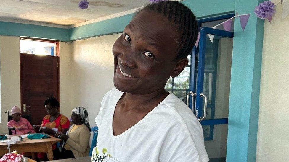 A woman in a white shirt has her head at an angle smiling at the camera