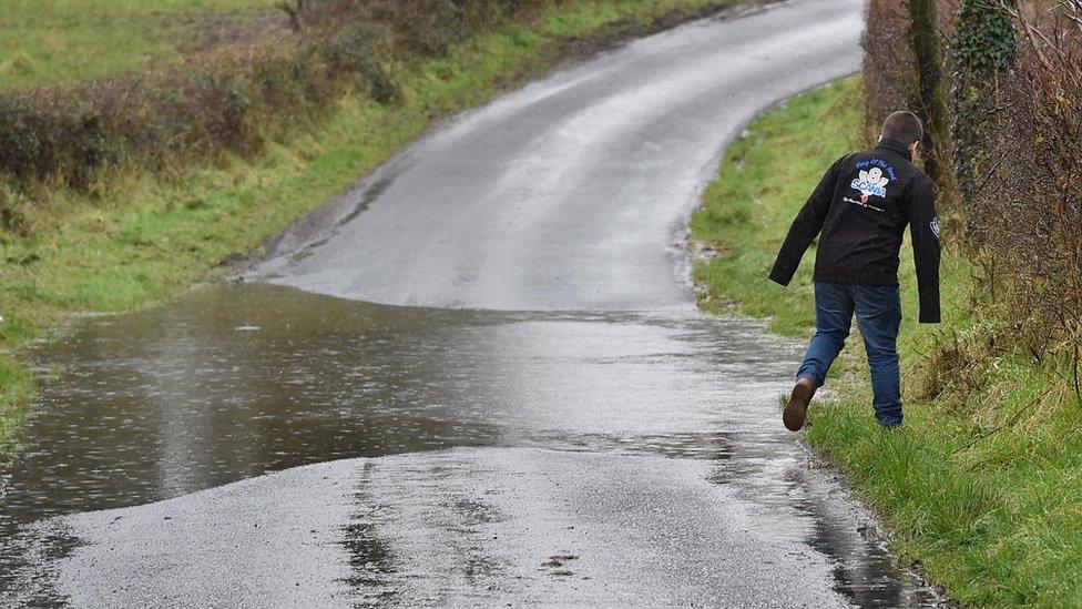 A pedestrian walks on grass verge to avoid flood