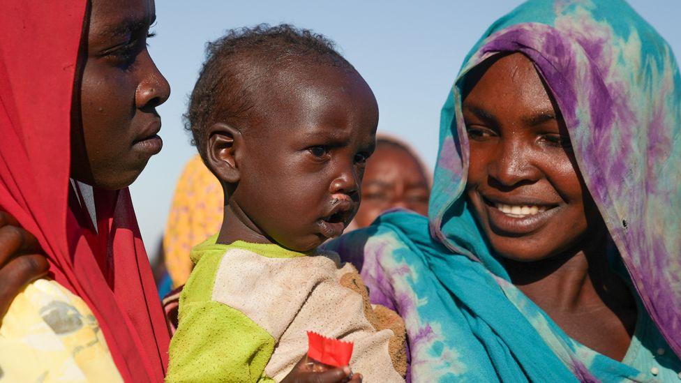 A woman with a green and purple headscarf smiles at a baby that she is holding.