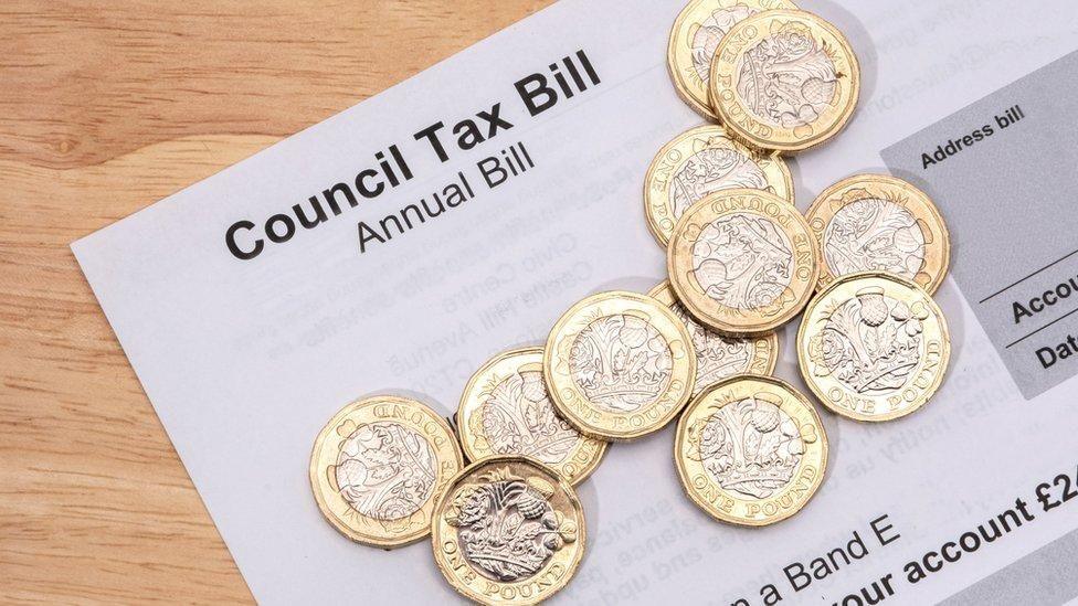 A pile of pound coins on top of a council tax bill, which is lying on a table 