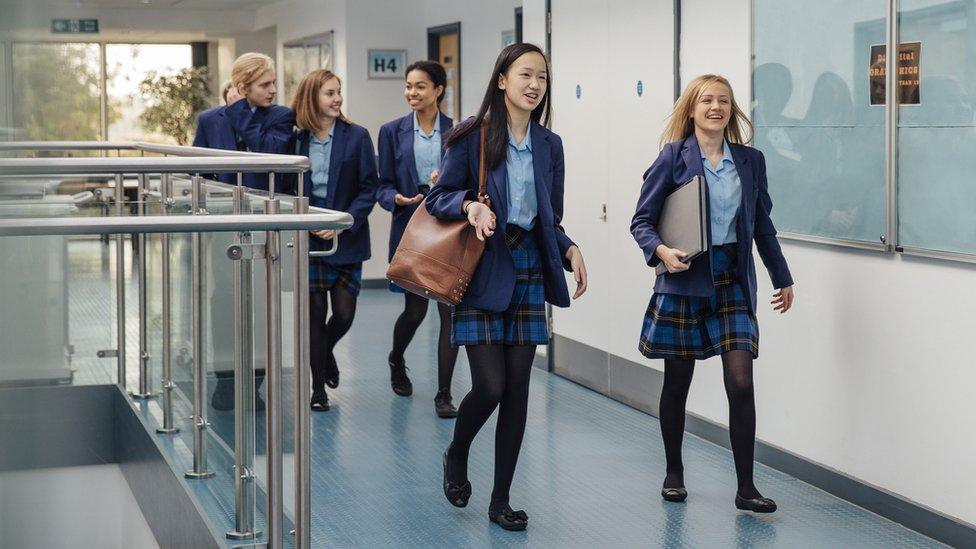 Group of students are walking down the school corridor together wearing uniform.