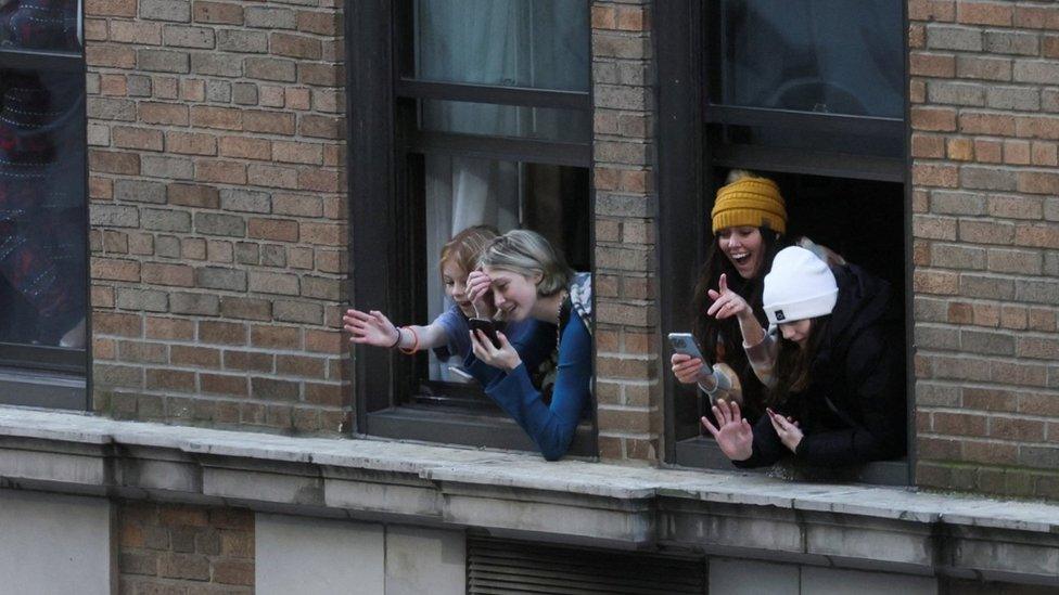 People look through their windows to watch the Macy's Thanksgiving Day Parade in the street