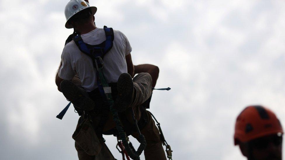 Utility workers wrapped around one another in a harness