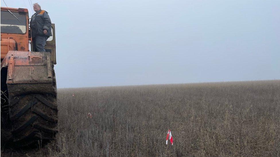 Man standing on tractor, flag in field