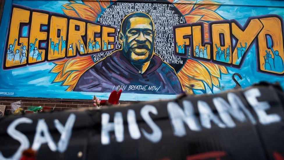 A man kneels and holds up his fist at a memorial site