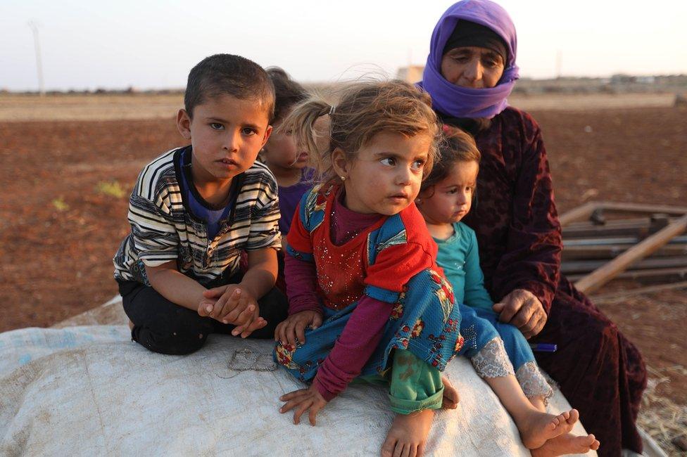 Syrian children and a woman sit near a camp for displaced civilians in Idlib province, Syria (1 September 2018)