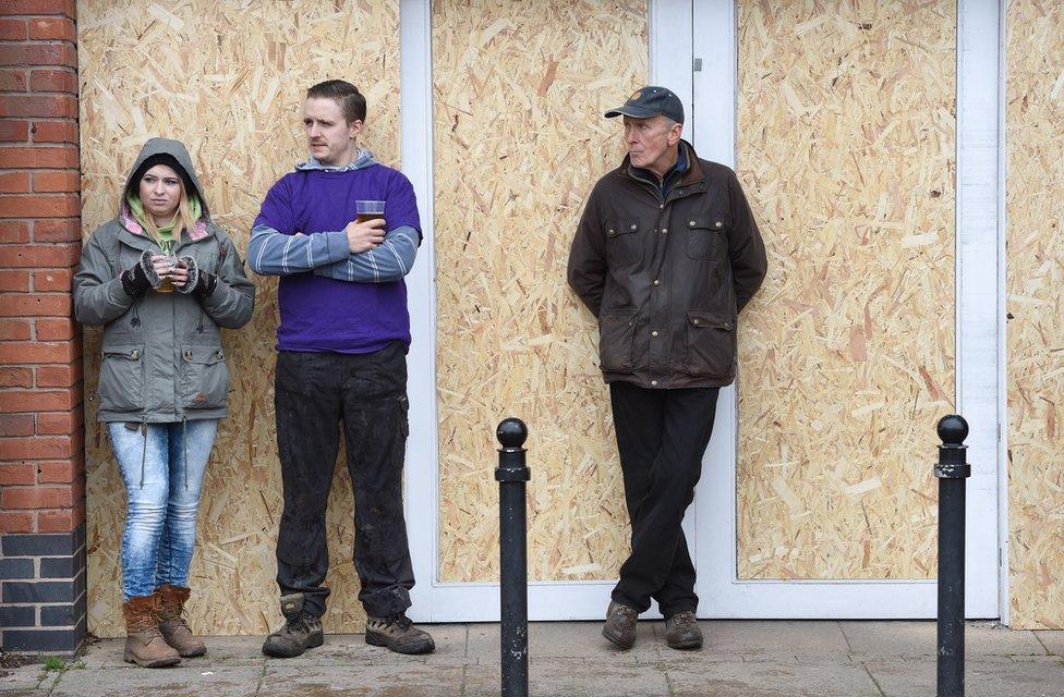 People stand in front of a boarded up shop in Ashbourne, Derbyshire, ahead of the Royal Shrovetide Football match