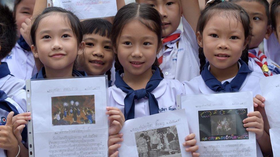 Thai students smile as they hold pictures of 12 boys and a football coach at a school in front of hospital where the boys rescued