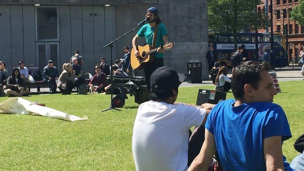 A busker sings songs of defiance in Piccadilly Gardens, Manchester, the day after a suicide bomber killed 22 people